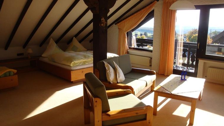 Ein gemütliches Dachzimmer mit einem großen Fenster und Blick auf die Landschaft. Das Zimmer ist mit einem Bett, einer Couch und einem Tisch ausgestattet.