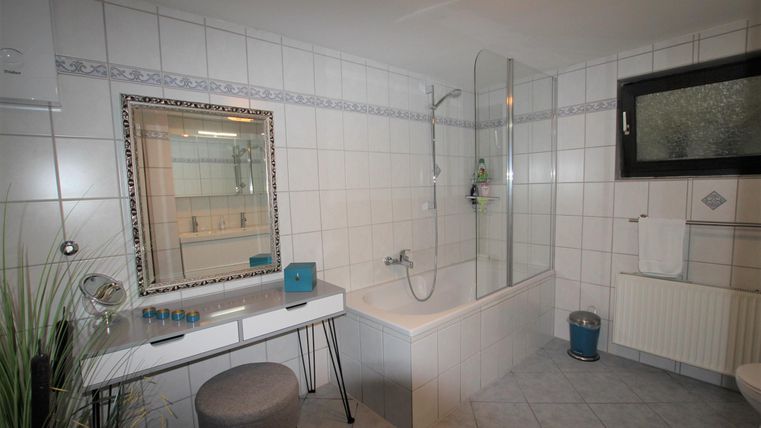 Ein modernes Badezimmer mit einer Dusche und einer Badewanne. Ein großer Spiegel und eine stilvolle Sitzgelegenheit runden das Bild ab.