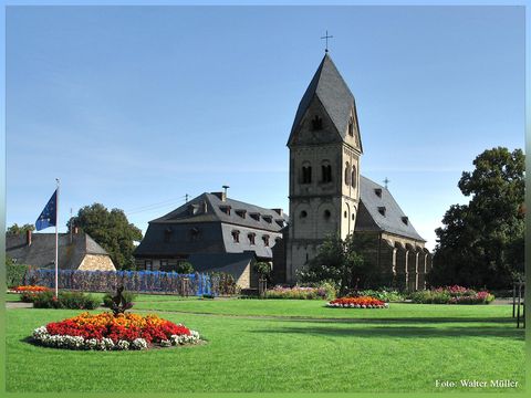 A beautiful church surrounded by a well-maintained garden with colorful flowers. The sky is clear and blue, creating a pleasant atmosphere.