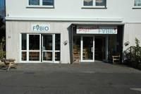 Ein Geschäft mit zwei Eingängen, eines mit dem Namen "Pöbio". Die Fassade ist hell und modern, umgeben von einem klaren Himmel.