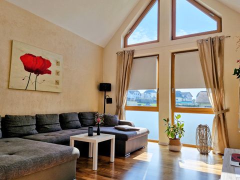 Ein helles Wohnzimmer mit großen Fenstern und schöner Aussicht. Ein gemütliches Sofa und eine Pflanze ergänzen den Raum.