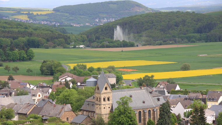 Eine malerische Landschaft mit sanften Hügeln und grünen Feldern. Im Vordergrund steht eine schöne Kirche in einem kleinen Dorf.