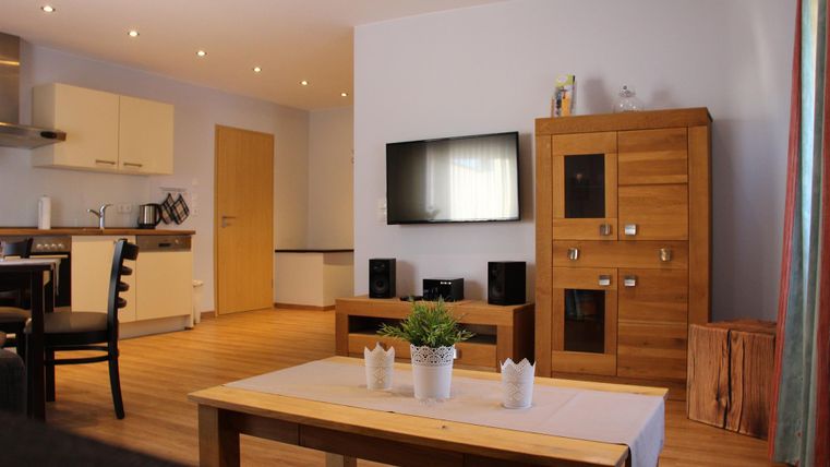 Ein modernes Wohnzimmer mit Holzmöbeln und einem großen Fernseher an der Wand. Die gemütliche Einrichtung schafft eine einladende Atmosphäre.