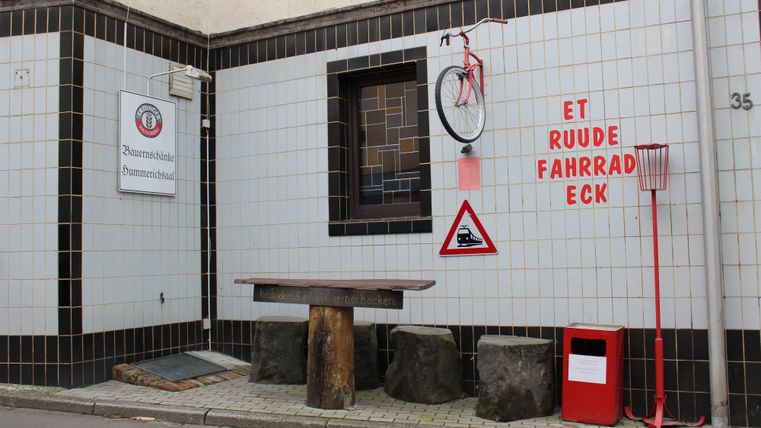 Ein fröhlicher Fahrradtreffpunkt mit einer bunten Wandgestaltung. Es gibt einen Tisch aus Holz und verschiedene Verkehrszeichen zur Sicherheit.