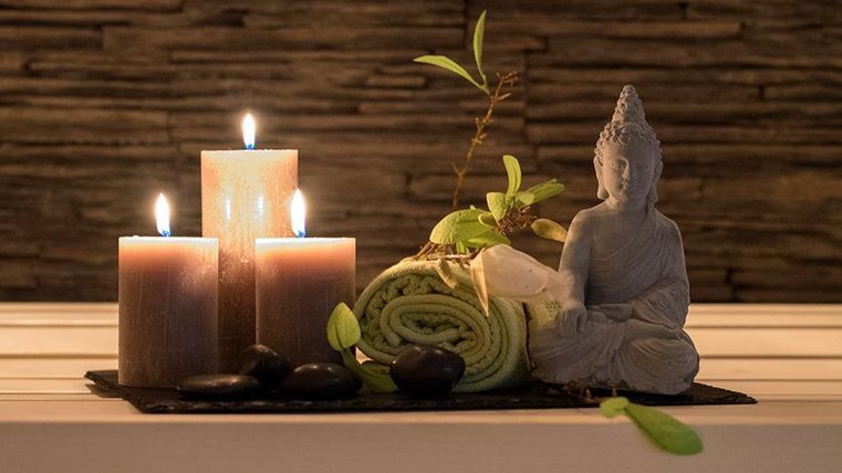 Eine entspannende Dekoration mit Kerzen, einem Buddha-Statuette und einem Handtuch. Die Stillleben schaffen eine friedliche Atmosphäre.