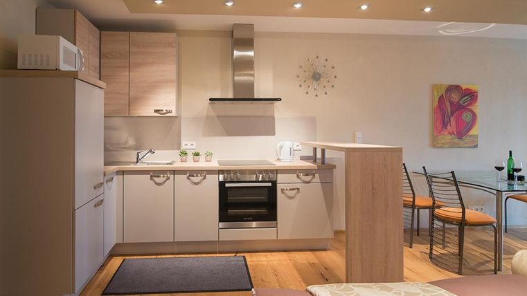 Eine moderne Küchenecke mit hellen Holzschränken und einem klaren Design. Der Raum ist offen und einladend, mit einem kleinen Tisch und Stühlen.