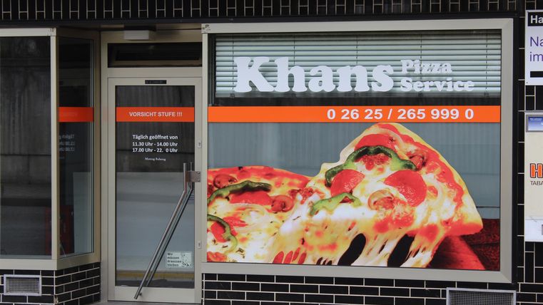 Ein Pizzaladen mit dem Namen "Khans Pizza Service". Die Fenster zeigen große Bilder von leckeren Pizzen.