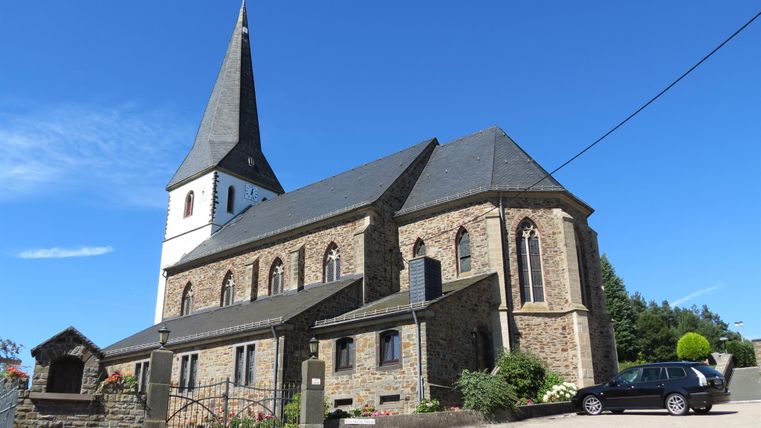 Pfarrkirche in Reifferscheid mit spitzem Turm und blauen Himmel.