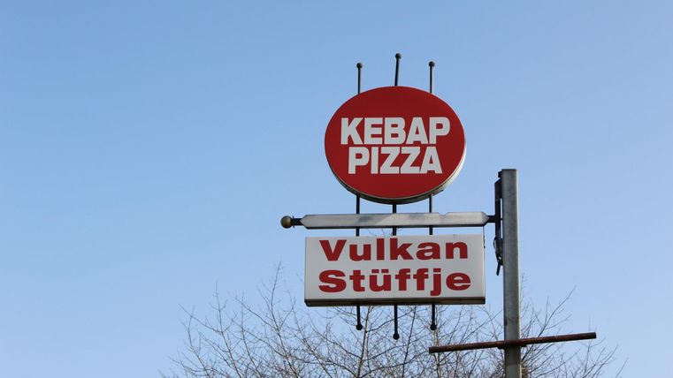 A sign with the inscription "Kebap Pizza" and "Vulkan Stüffje". The background is a clear blue sky.