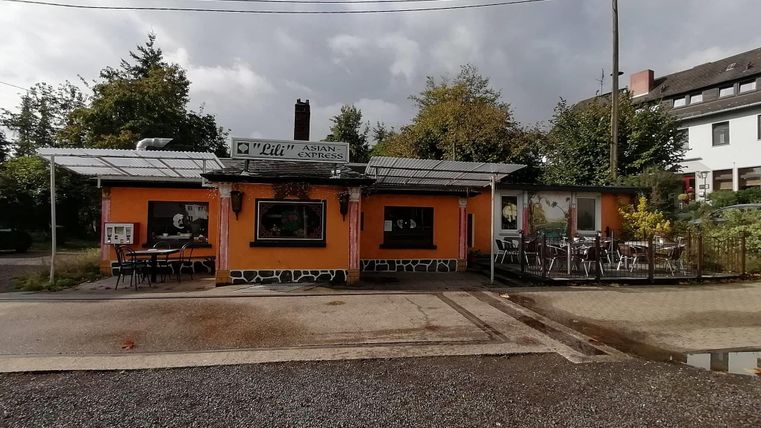 Ein gemütliches Restaurant mit oranger Fassade und Tischen im Freien. Umgeben von Bäumen und einer ruhigen Straße.