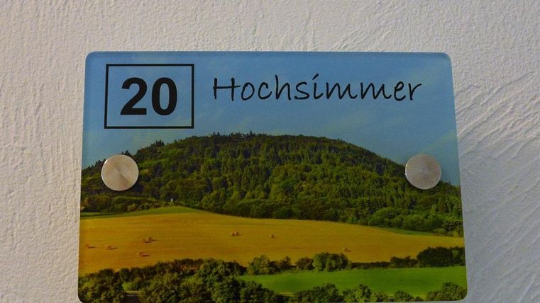 Ein Schild mit der Nummer 20 und dem Schriftzug "Hochsimmer". Im Hintergrund ist eine grüne Landschaft mit Hügeln und Feldern zu sehen.