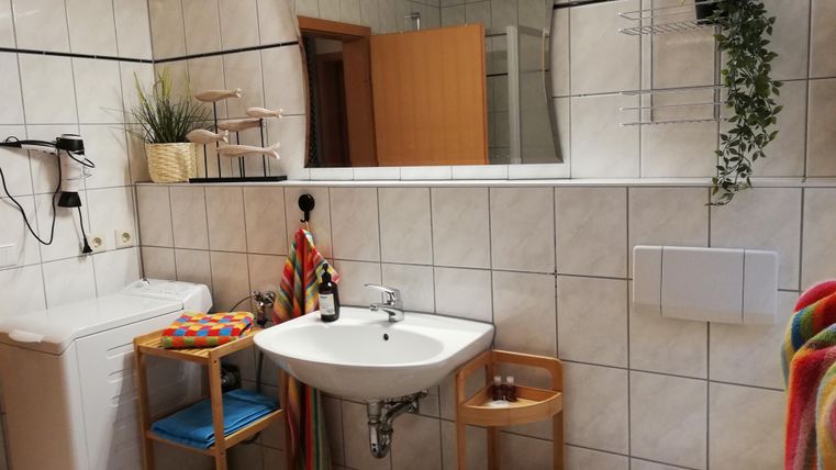 A modern bathroom with a sink, a mirror, and a washing machine. There are colorful towels and plants that create an inviting atmosphere.