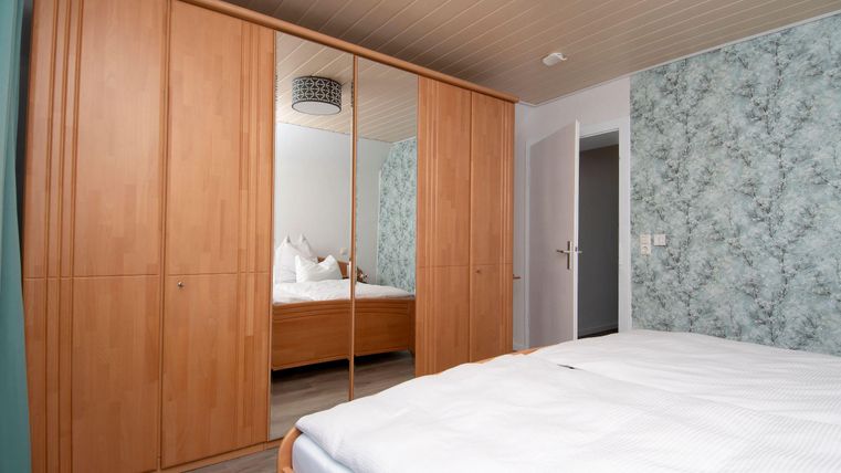 Ein modernes Schlafzimmer mit einem großen Holzschrank und einem Bett. Die Wände sind in sanften Farben gehalten, und es gibt eine angenehme Beleuchtung.