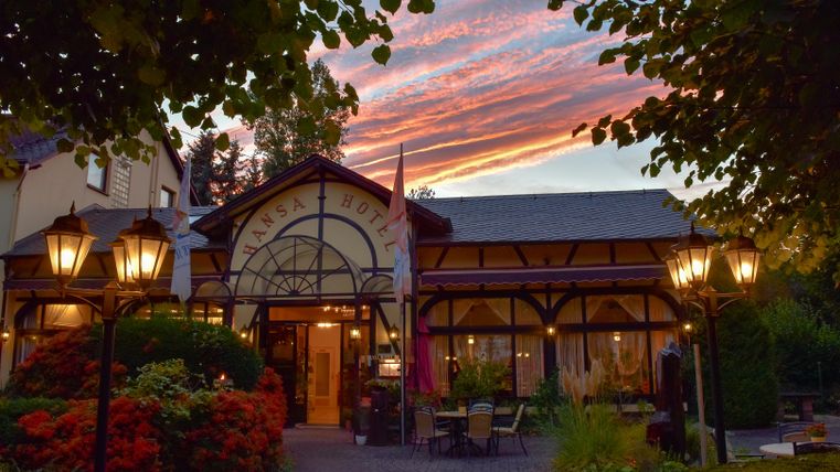 Ein charmantes Hotel mit einer einladenden, historischen Fassade und romantischen Laternen. Der Himmel ist in warmen Farben während des Sonnenuntergangs gefärbt.