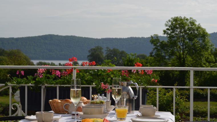 Ein schöner Frühstückstisch auf einem Balkon mit Blick auf die Berge. Der Tisch ist liebevoll gedeckt mit Früchten, Getränken und frischen Brötchen.