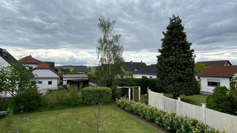 Ein ruhiger Garten mit Rasen und einigen Bäumen. Im Hintergrund sind Wohnhäuser und ein bewölkter Himmel zu sehen.