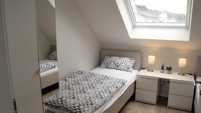 Ein gemütliches Schlafzimmer mit einem Einzelbett und einem modernen Design. Das Zimmer hat ein Dachfenster und zwei Nachttische mit Lampen.