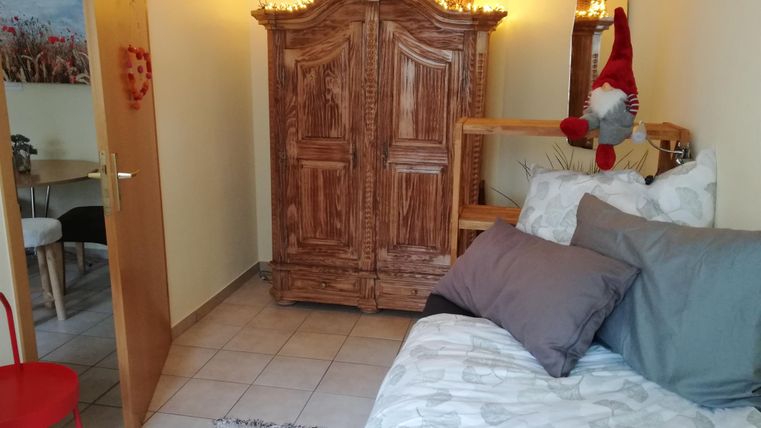A cozy room with a wooden cabinet and a comfortable bed. In the background, a table and chairs are visible.