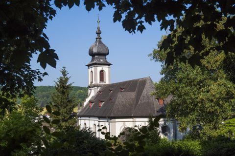 Eine malerische Kirche mit einem charakteristischen Turm, umgeben von Bäumen. Der strahlend blaue Himmel verleiht der Szene eine ruhige Atmosphäre.