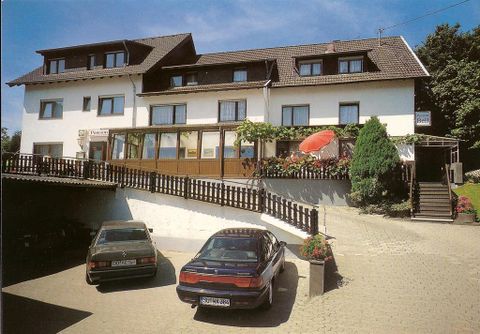 Ein charmantes Hotel mit einem großen Außenbereich und einem schönen Garten. Vor dem Gebäude stehen zwei Autos auf einem gepflasterten Parkplatz.