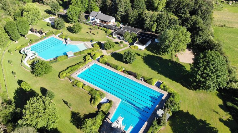 Ein schöner Außenpoolbereich mit zwei großen Schwimmbecken. Umgeben von viel Grün und Bäumen in einer ruhigen Landschaft.