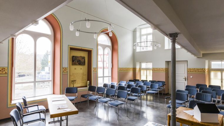 A bright room with chairs and large windows. A table is in the foreground, and the walls are tastefully decorated.