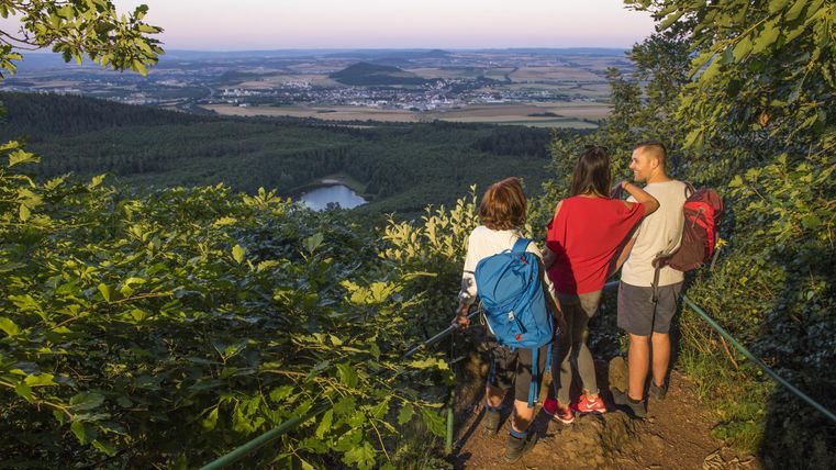 Eine Gruppe von Wanderern schaut auf eine wunderschöne Landschaft. Der Sonnenuntergang beleuchtet die sanften Hügel im Hintergrund.