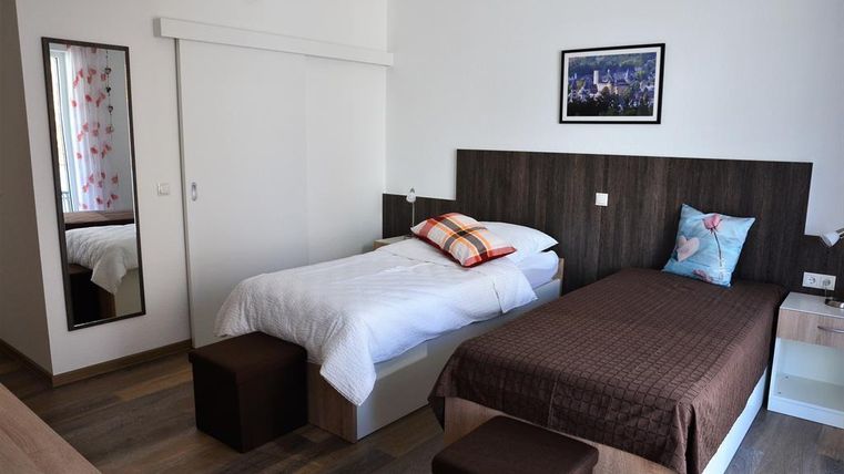 Ein helles Schlafzimmer mit zwei Betten und einem minimalistischen Design. An der Wand hängt ein Bild, und es gibt einen großen Spiegel, der den Raum erweitert.