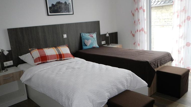 Ein helles Schlafzimmer mit zwei Einzelbetten, einem modernen Nachttisch und einer schönen Aussicht durch große Fenster. Die Wände sind mit hellen Vorhängen und einem dekorativen Bild geschmückt.