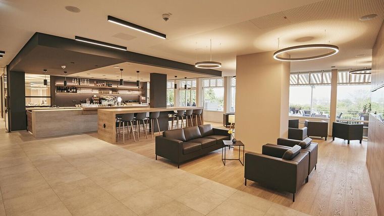 Ein modernes und elegantes Interieur mit einem gemütlichen Sitzbereich und einer Bar. Große Fenster sorgen für viel Tageslicht und eine einladende Atmosphäre.