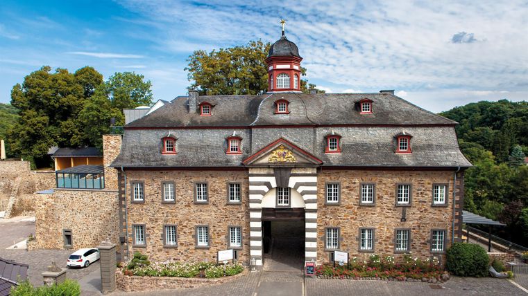 A historical building with a distinctive facade and a small tower. Surrounded by trees and a clear sky.