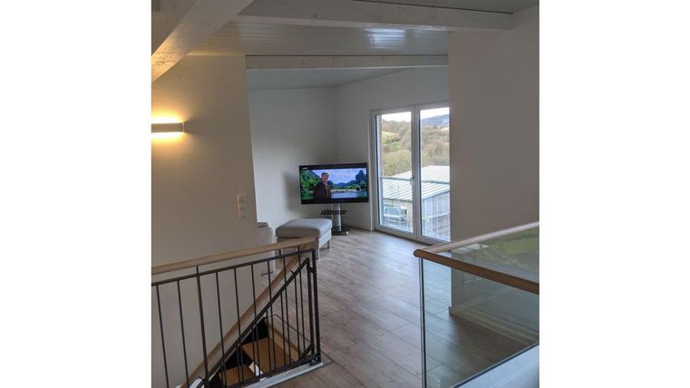 Ein moderner Wohnraum mit Holzfußboden und großen Fenstern. Ein Fernseher steht in der Ecke und bietet einen Blick nach draußen.
