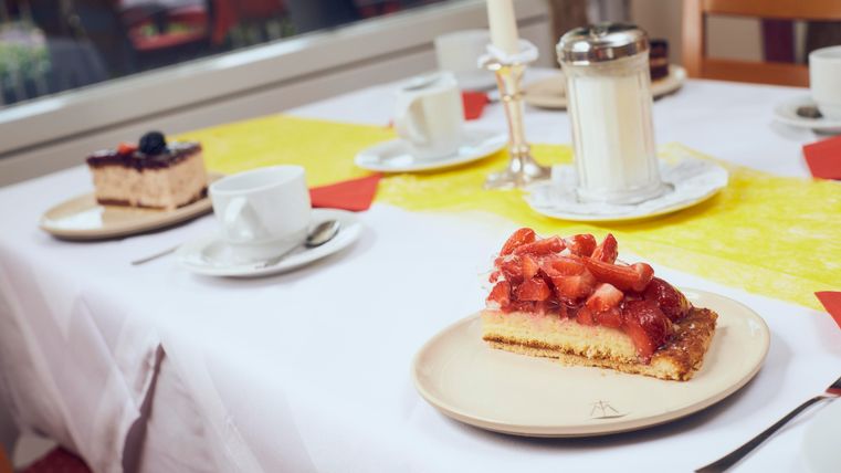 A set table with two pieces of cake, one with strawberries and one with blueberries. There are cups, a candlestick, and a milk jug.