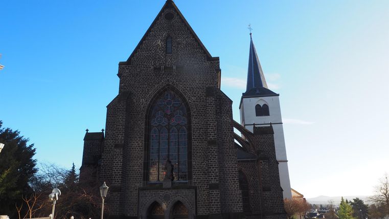 An old church with a tall tower and colorful windows. The sky is clear and blue.