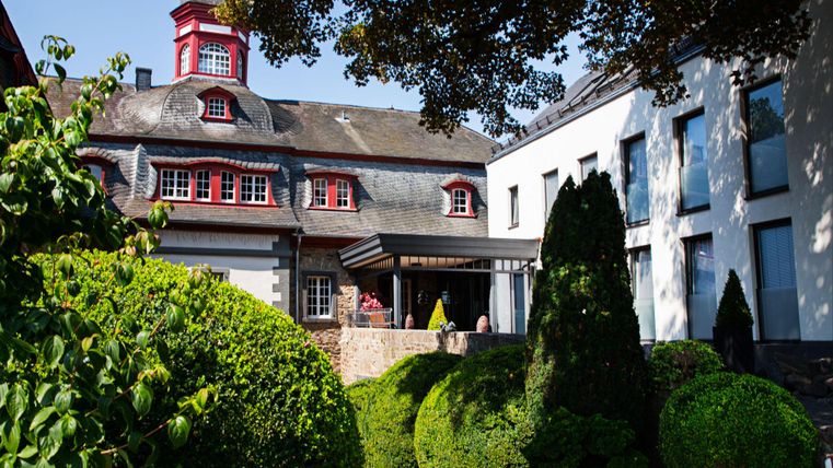 Eine malerische Restaurantansicht mit grünem Garten und stilvoller Architektur. Der Himmel ist klar und die Umgebung ist einladend.