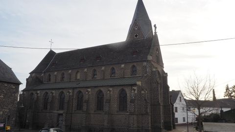 Eine alte Kirche mit einem markanten Turm und gotischen Fenstern. Die Fassade ist aus grauem Stein und vermittelt einen historischen Eindruck.