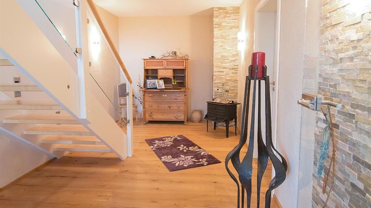 Ein heller Eingangsbereich mit Holzfußboden und einer modernen Treppe. An der Wand befindet sich ein dekorativer Stein, und ein stilvolles Möbelstück steht in der Ecke.