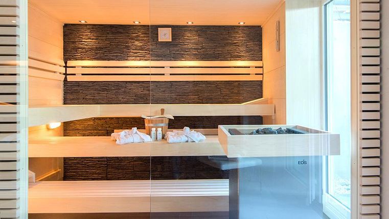 Eine moderne Sauna mit hellen Holzwänden und eleganten Steinelementen. Handtücher und Pflegeprodukte liegen bereit für einen entspannenden Aufenthalt.