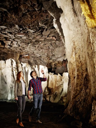 Ein Paar steht in einer beeindruckenden Höhle und schaut auf die Felsformationen. Die Wände sind beleuchtet und zeigen interessante Strukturen.