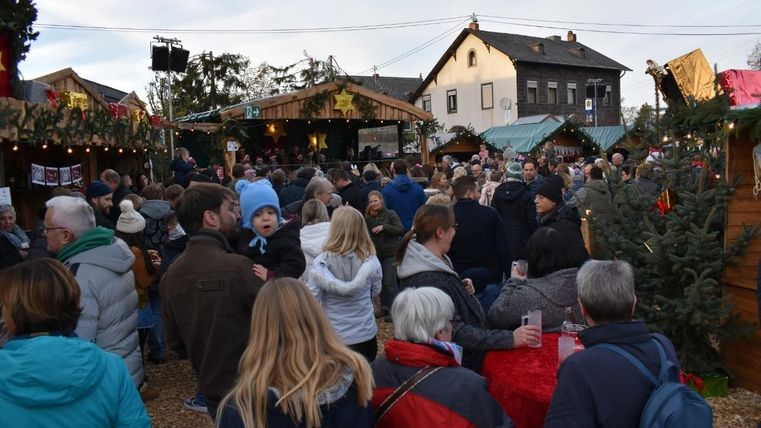 Ein belebter Weihnachtsmarkt mit vielen Besuchern. Bunte Stände und festliche Dekorationen schaffen eine fröhliche Atmosphäre.