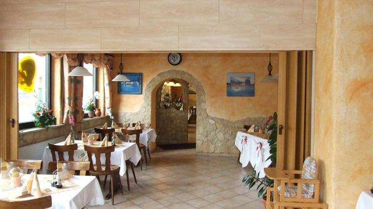 An inviting restaurant with tables and chairs. The walls are painted in warm colors and there are artworks on the walls.