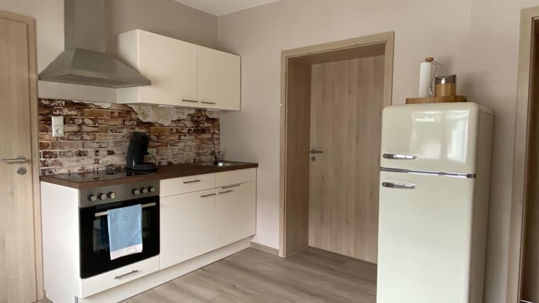 Eine moderne Küche mit weißen Möbeln und einer Steinwand. Der Kühlschrank ist grün und die Küche ist gut beleuchtet.