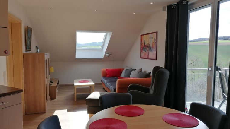 A bright and modern living room with a cozy sofa and a dining table. Large windows offer a beautiful view outside.