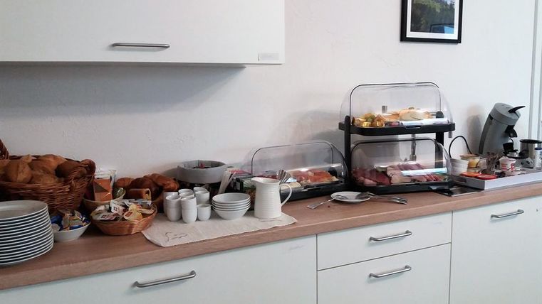 Ein Büffet mit verschiedenen Frühstückszutaten, einschließlich Brötchen, Marmelade und Käse. Es gibt auch eine Kaffeemaschine und verschiedene Tassen auf dem Tisch.