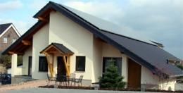 A modern single-family house with a flat roof and a wooden shelter. The garden is well-kept and there is an outdoor seating area.