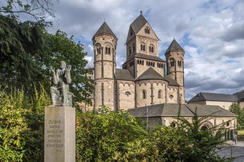 Eine beeindruckende Kirche mit markanten Türmen und einer grünen Umgebung. Im Vordergrund steht eine Statue.