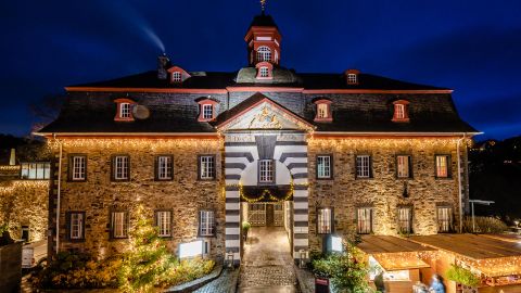 Ein historisches Gebäude mit feierlicher Beleuchtung bei Nacht. Die Fassade besteht aus Steinen und hat einen markanten Türmchen.