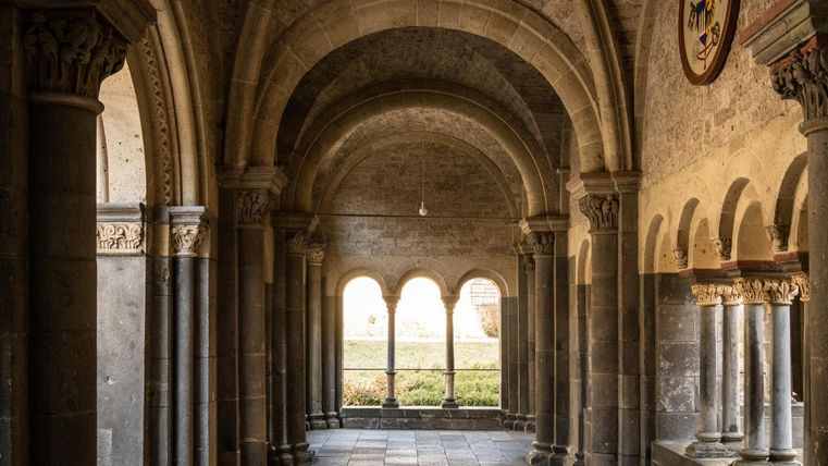 A historic courtyard with tall arches and columns. The light gently falls through the windows and illuminates the stone walls.