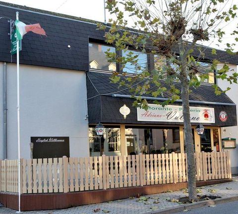 Ein italienisches Restaurant mit einem Holzgeländer und einer Flagge. Die Fassade ist modern und einladend, mit großen Fenstern.