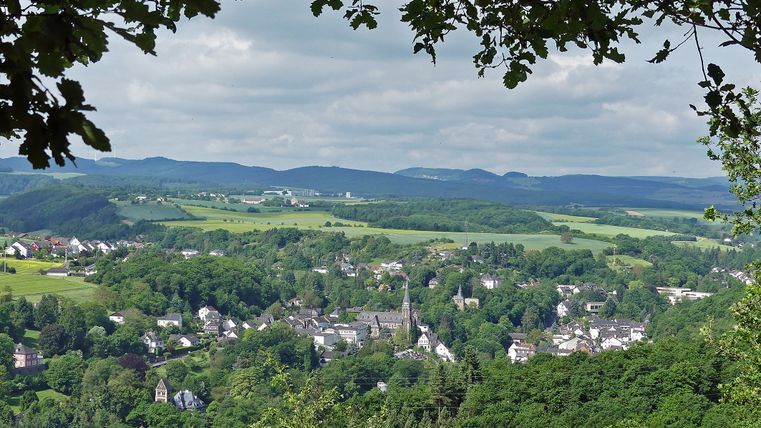 Panoramablick auf Burgbrohl mit Kirche im Zentrum, umgeben von grüner Landschaft und Hügeln.